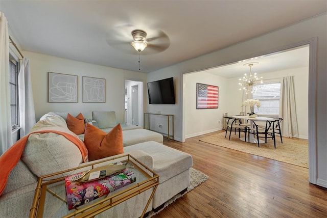 living room with baseboards, wood finished floors, and ceiling fan with notable chandelier