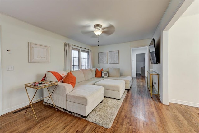 living room featuring a ceiling fan, visible vents, wood finished floors, and baseboards