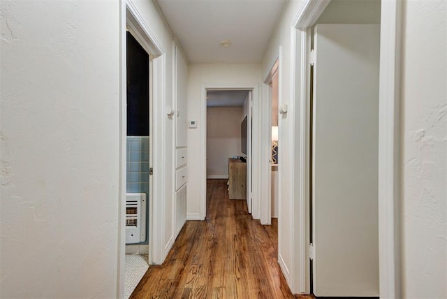 hallway with heating unit, wood finished floors, and a textured wall