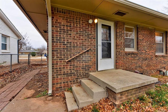 view of exterior entry featuring brick siding and fence