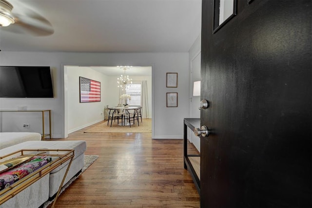 living room featuring ceiling fan with notable chandelier, wood finished floors, and baseboards