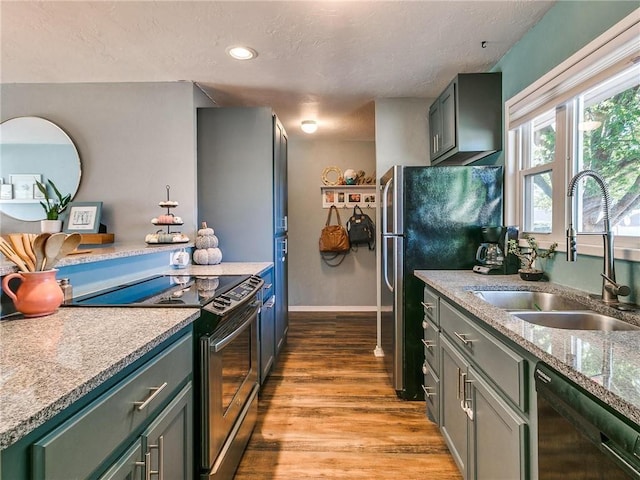 kitchen with stainless steel appliances, sink, light stone counters, and light hardwood / wood-style floors