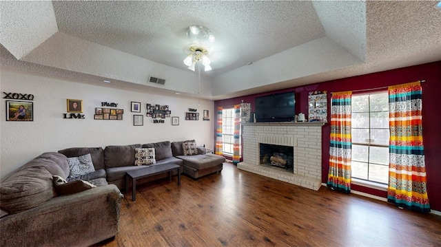 living room featuring a raised ceiling, a textured ceiling, a fireplace, and dark hardwood / wood-style flooring