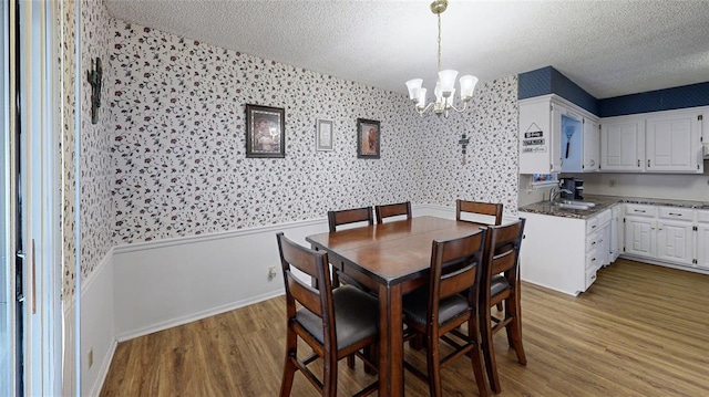 dining space featuring an inviting chandelier, sink, light hardwood / wood-style floors, and a textured ceiling