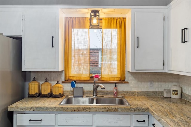 kitchen with tasteful backsplash, white cabinetry, sink, and stainless steel fridge