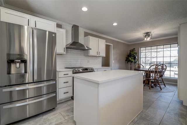 kitchen with white cabinetry, ornamental molding, appliances with stainless steel finishes, a kitchen island, and wall chimney range hood