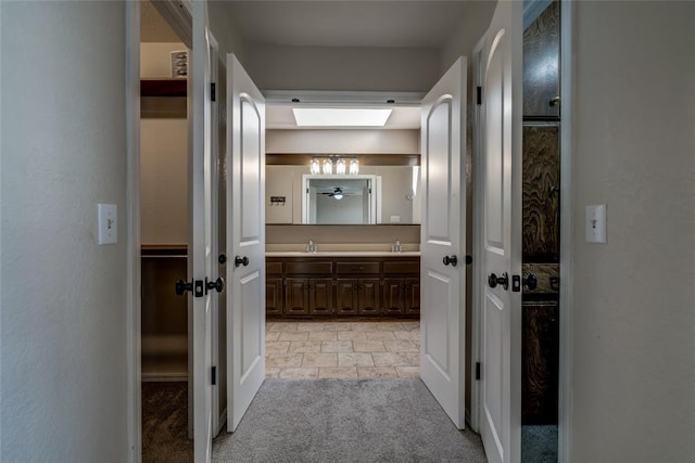 hallway featuring light colored carpet, a skylight, and sink