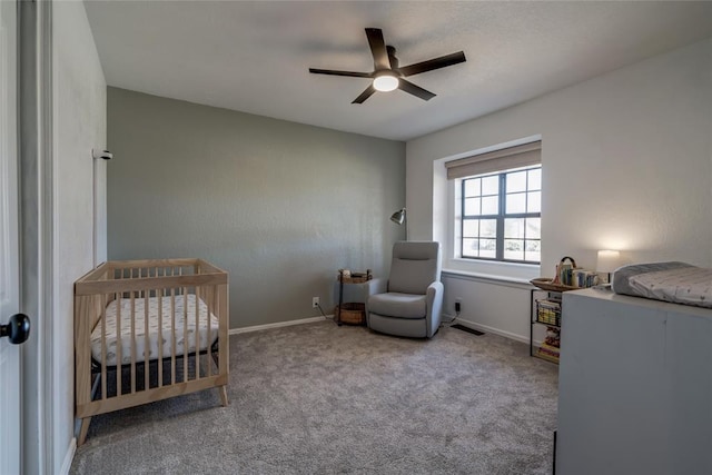 bedroom with light colored carpet, a nursery area, and ceiling fan