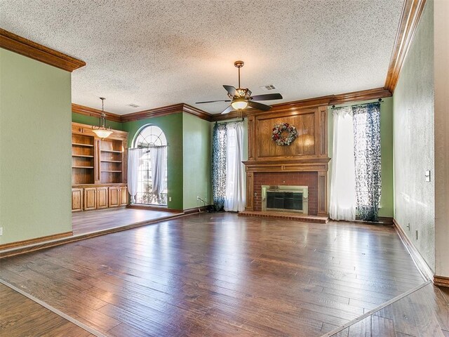 unfurnished living room featuring dark hardwood / wood-style flooring, ornamental molding, ceiling fan, a brick fireplace, and a textured ceiling