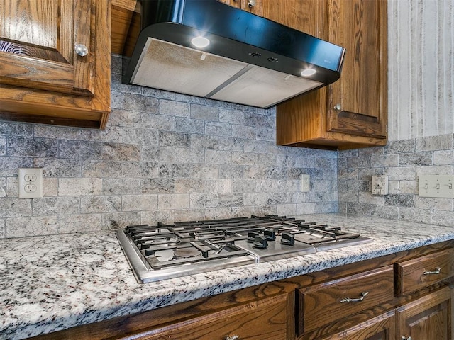 kitchen featuring tasteful backsplash, stainless steel gas cooktop, exhaust hood, and light stone counters