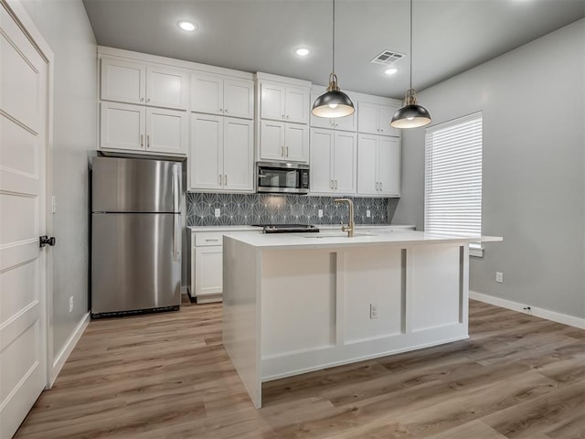 kitchen featuring an island with sink, appliances with stainless steel finishes, white cabinets, and decorative backsplash