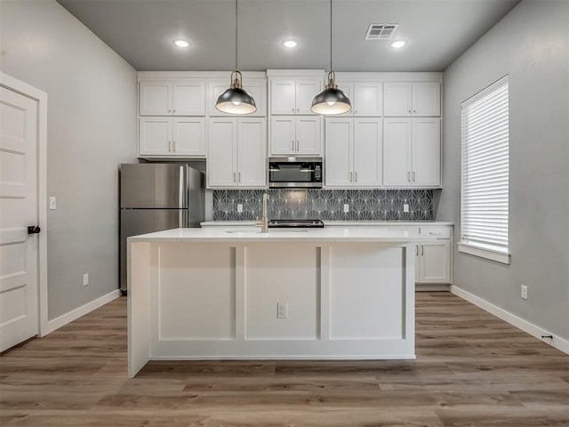 kitchen with decorative light fixtures, stainless steel appliances, an island with sink, and white cabinets