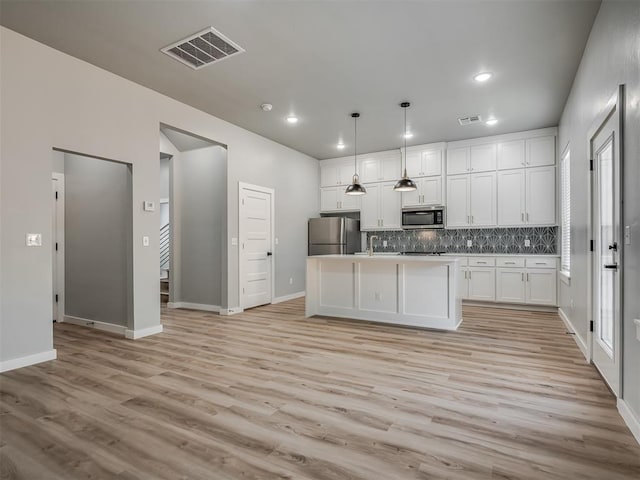 kitchen with hanging light fixtures, stainless steel appliances, white cabinets, a center island with sink, and decorative backsplash