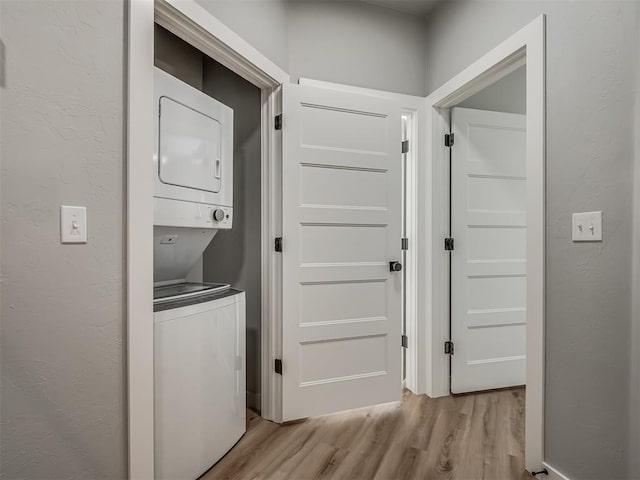 clothes washing area featuring stacked washer and dryer and light hardwood / wood-style flooring