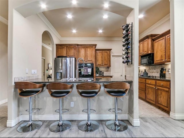 kitchen with ornamental molding, a kitchen breakfast bar, and black appliances