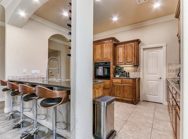 kitchen featuring sink, crown molding, light tile patterned floors, black oven, and backsplash