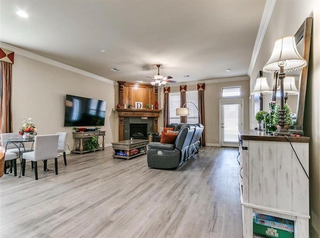 living room featuring ornamental molding, a large fireplace, ceiling fan, and light hardwood / wood-style floors