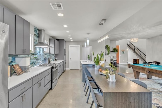 kitchen featuring decorative light fixtures, stainless steel gas range oven, a center island, and wall chimney exhaust hood