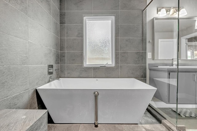 bathroom featuring vanity, a tub to relax in, a healthy amount of sunlight, and tile walls