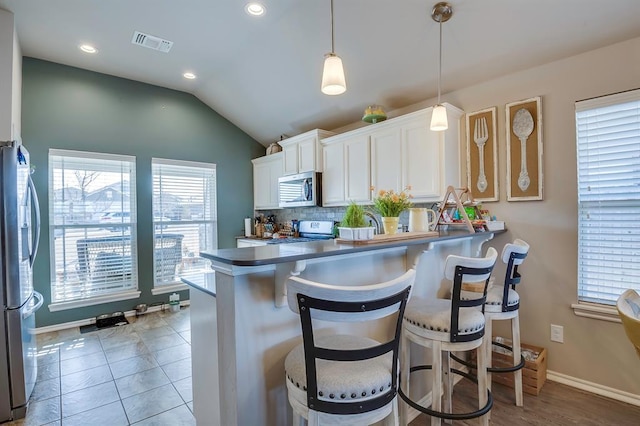 kitchen with stainless steel appliances, a kitchen bar, kitchen peninsula, and white cabinets