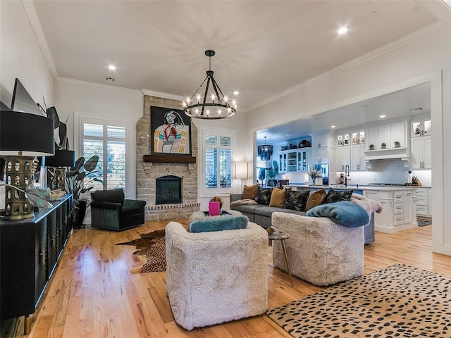 living room with ornamental molding, a stone fireplace, sink, and light hardwood / wood-style flooring