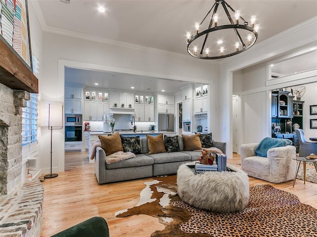 living room with ornamental molding, a stone fireplace, a notable chandelier, and light hardwood / wood-style flooring