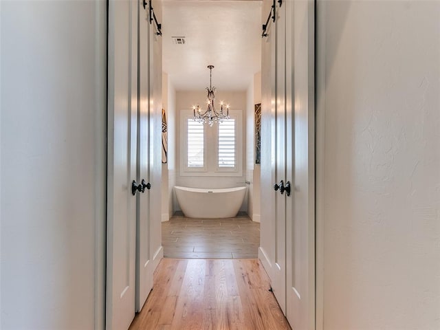 hallway featuring a notable chandelier, a barn door, and light wood-type flooring