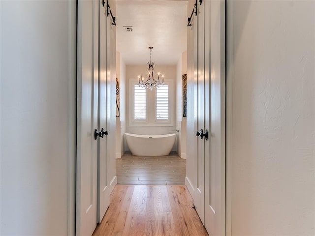 3208 Rolling Woods Dr, Norman, OK 73072 - bathroom with visible vents, baseboards, wood finished floors, a freestanding tub, and a notable chandelier