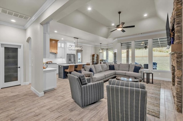 living room featuring crown molding, ceiling fan with notable chandelier, a raised ceiling, and light wood-type flooring