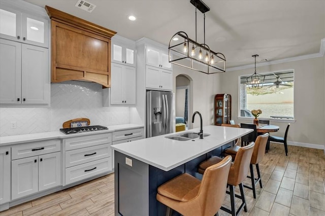 kitchen with sink, a kitchen island with sink, stainless steel appliances, white cabinets, and decorative light fixtures