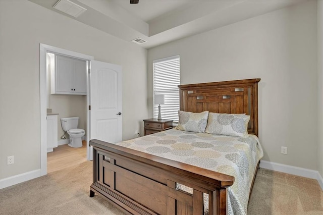 carpeted bedroom with connected bathroom and a tray ceiling