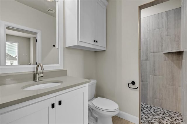 bathroom featuring vanity, a tile shower, and toilet