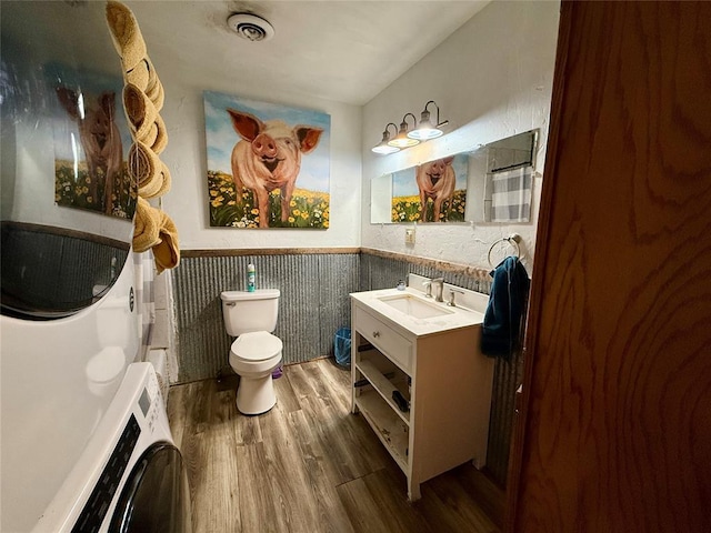 bathroom with vanity, stacked washer and dryer, hardwood / wood-style flooring, and toilet