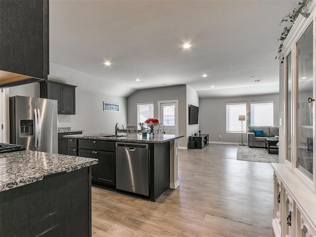 kitchen with stone counters, a center island with sink, a wealth of natural light, stainless steel appliances, and light hardwood / wood-style floors