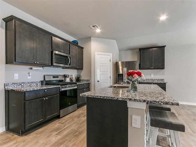 kitchen with a kitchen island with sink, light stone countertops, and appliances with stainless steel finishes