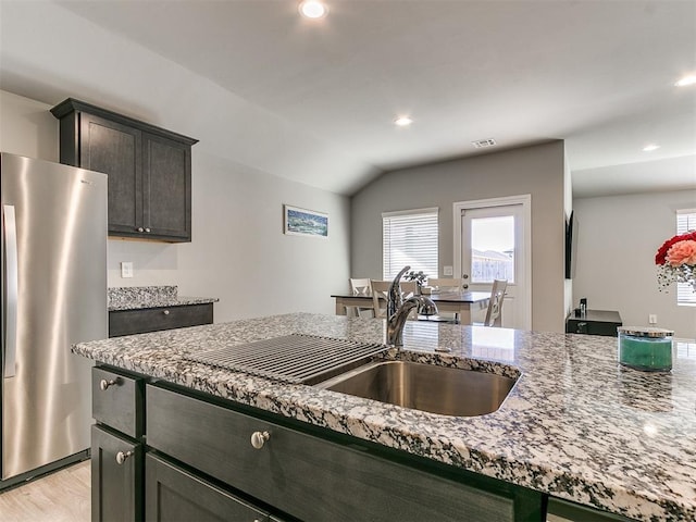 kitchen featuring sink, stainless steel fridge, light stone counters, light hardwood / wood-style floors, and dark brown cabinets