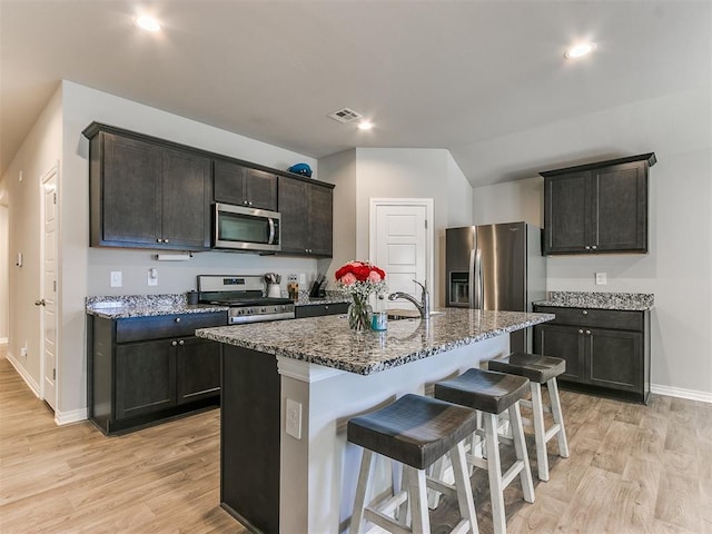 kitchen featuring stainless steel appliances, a kitchen bar, a kitchen island with sink, and light wood-type flooring