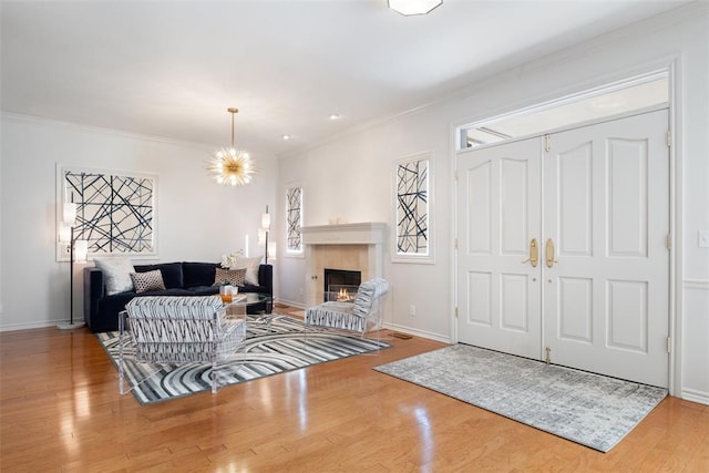 entryway with a tile fireplace, wood-type flooring, a chandelier, and crown molding