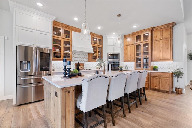 kitchen with stainless steel appliances, a center island, light hardwood / wood-style floors, decorative light fixtures, and custom exhaust hood