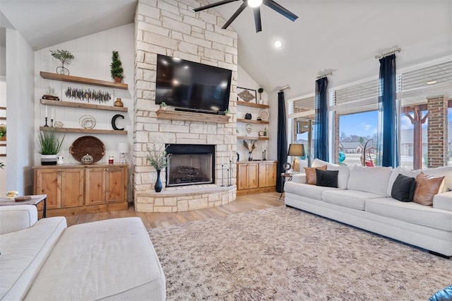 living room featuring a stone fireplace, high vaulted ceiling, ceiling fan, light wood-type flooring, and built in shelves