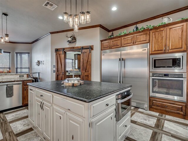 kitchen featuring built in appliances, white cabinets, a kitchen island, decorative light fixtures, and a barn door