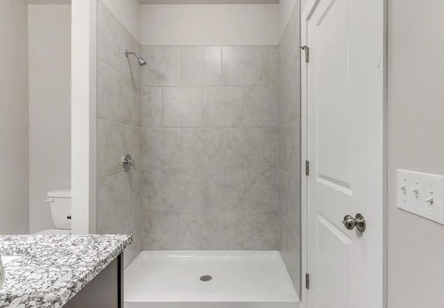 bathroom with vanity, a tile shower, and toilet