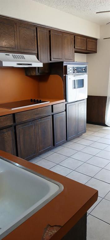 kitchen with black electric stovetop, light tile patterned floors, dark brown cabinetry, white oven, and a textured ceiling