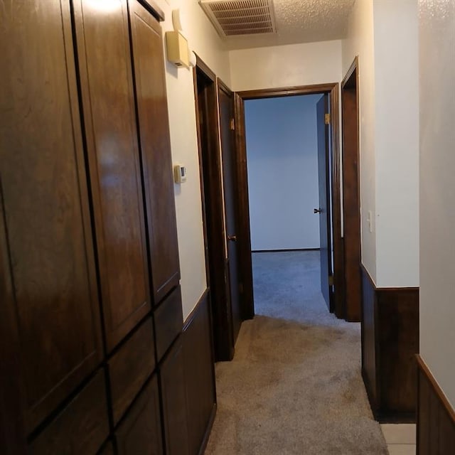 hall with light colored carpet and a textured ceiling