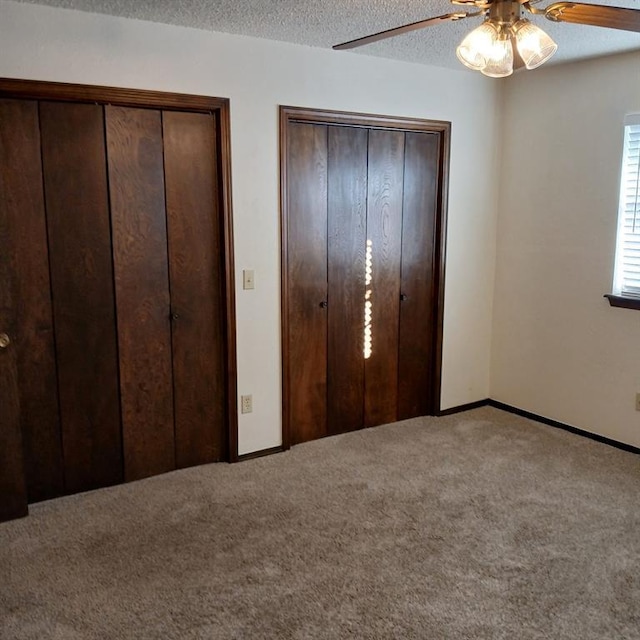 unfurnished bedroom featuring ceiling fan, a textured ceiling, multiple closets, and carpet