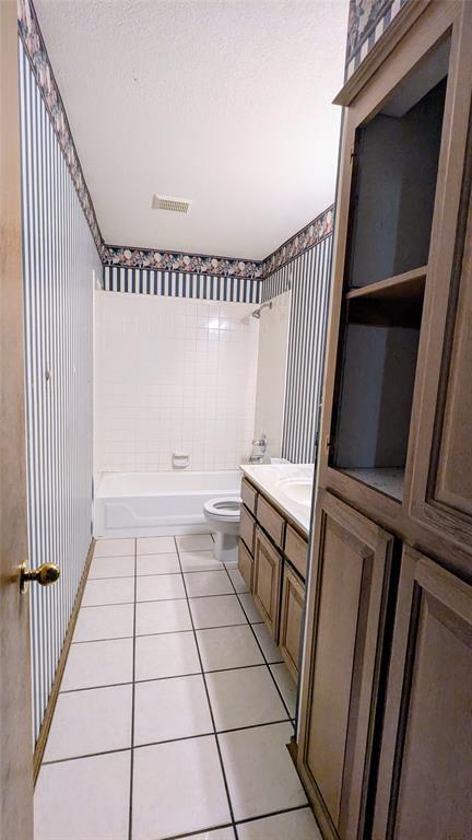 full bathroom with tiled shower / bath, vanity, toilet, tile patterned floors, and a textured ceiling