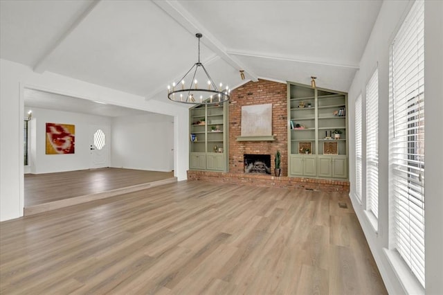 unfurnished living room featuring an inviting chandelier, lofted ceiling with beams, built in features, hardwood / wood-style flooring, and a fireplace