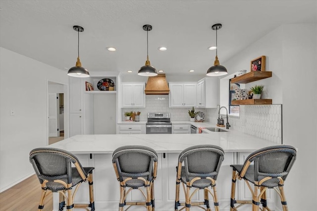 kitchen featuring pendant lighting, appliances with stainless steel finishes, white cabinets, a kitchen bar, and custom exhaust hood