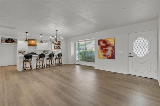 interior space with pendant lighting, a breakfast bar, white cabinetry, light hardwood / wood-style floors, and custom range hood