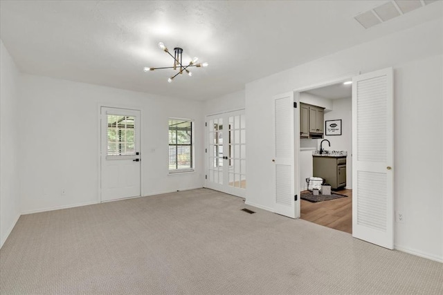 carpeted empty room featuring an inviting chandelier and french doors